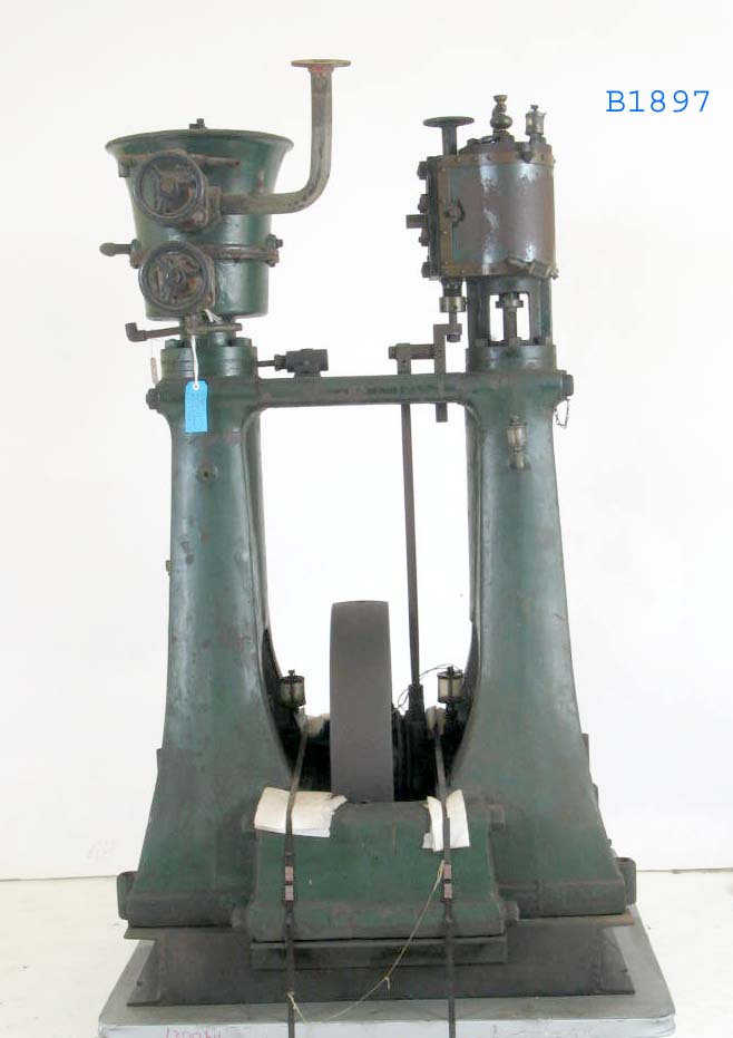 A museum artefact comprised of two painted metal towers. At their base and between the towers sits a wheel. At the top of each tower are various gears, knobs and levers.